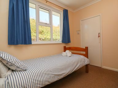 A bedroom with a single bed striped bedding blue curtains and a closed door at The Shack in Mawgan Porth near Newquay
