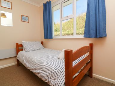 A bedroom with a wooden single bed with striped bedding and blue curtains on a window at The Shack in Mawgan Porth near Newquay