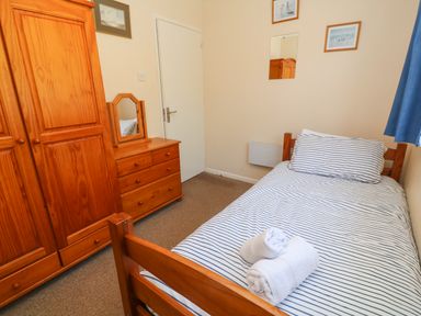 A bedroom with a bed with striped bedding a wooden wardrobe and chest of drawers with a mirror at The Shack in Mawgan Porth near Newquay