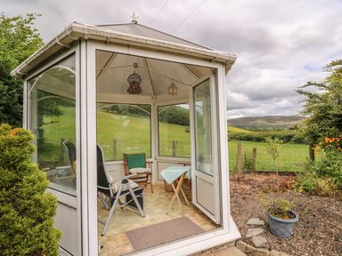 A small garden gazebo with chairs and a table in a rural grassy area at Penlone Cottage in Rhayader