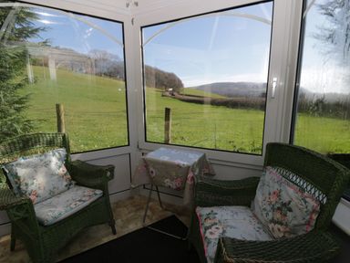 A conservatory with green chairs and a table at Penlone Cottage in Rhayader