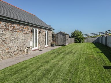 A grass lawn next to a stone wall house with a wooden shed and a fence at Middle Barn in Launceston
