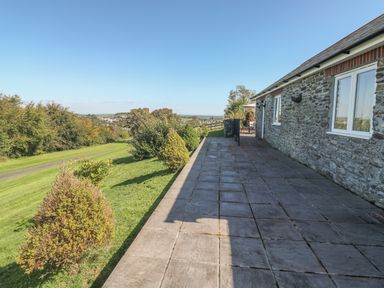 A stone house with a tiled patio and bushes along a grass lawn at Middle Barn in Launceston