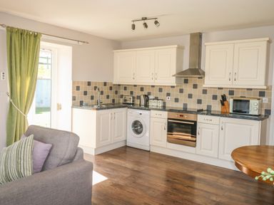 A kitchen with white cabinets black countertop washing machine oven and microwave at Middle Barn in Launceston
