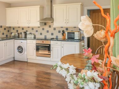 A kitchen with white cabinets appliances and a wooden dining table with flowers at Middle Barn in Launceston
