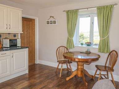 A kitchen area with wooden table and two chairs next to a window with green curtains at Middle Barn in Launceston