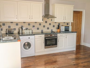 A kitchen with white cabinets a washing machine an oven a microwave and countertop appliances at Middle Barn in Launceston