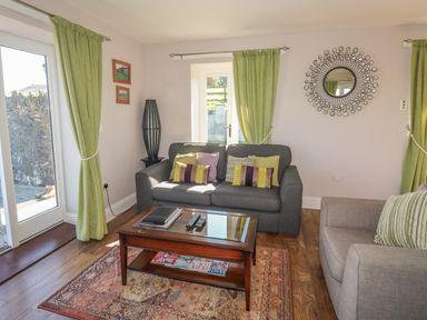 A living room with a gray sofa and armchair a wooden coffee table a decorative mirror and green curtains at Middle Barn in Launceston