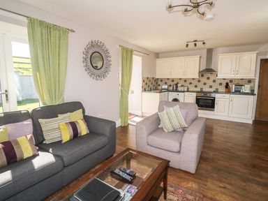 A living room with gray and light brown sofas and green curtains next to a kitchen with white cabinets and tiled backsplash at Middle Barn in Launceston