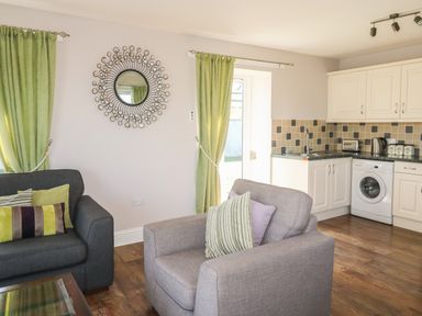 A living room with armchairs and green curtains next to a kitchen area with white cabinets at Middle Barn in Launceston