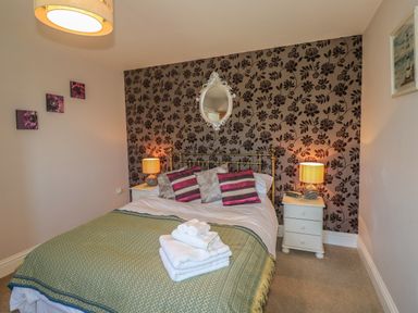 A bedroom with a bed folded towels on the bed two bedside tables with lamps and floral wallpaper at Middle Barn in Launceston