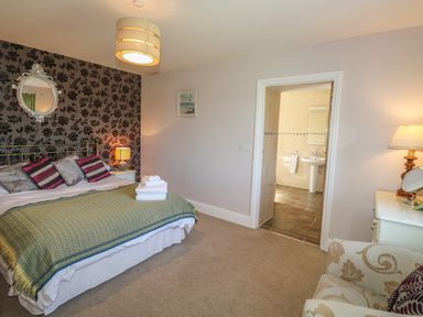 A bedroom with a double bed and patterned wallpaper and an open door to a bathroom at Middle Barn in Launceston