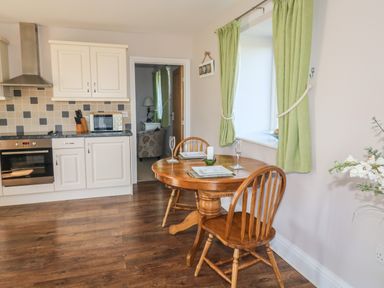 A kitchen area with white cabinets a wooden dining table set for two and green curtains at Middle Barn in Launceston