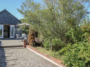 A garden with gravel path shrubs and a patio with table chairs and umbrella at Middle Barn in Launceston