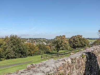 A stone wall with a wooden fence trees and a grassy field overlooking a village with a church tower at Middle Barn Launceston