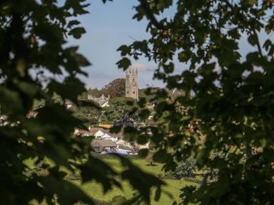 A view through trees of a village with a tall church tower and houses at Middle Barn in Launceston