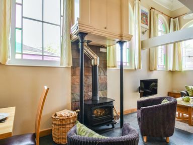 A living room with a wood stove flanked by two black columns and two armchairs near stained glass windows at The New Chapel in Great Hatfield near Hornsea