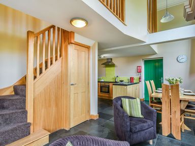 A living area with a wooden staircase, kitchen with green tiled backsplash, dining table, and purple chairs at The New Chapel in Great Hatfield near Hornsea