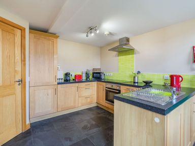 A kitchen with wooden cabinets black countertops a stove a sink and green tile backsplash at The New Chapel in Great Hatfield near Hornsea