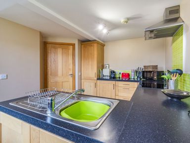 A kitchen with wooden cabinets a sink with a drying rack and green basin a coffee maker toaster and microwave at The New Chapel in Great Hatfield near Hornsea