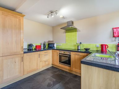 A kitchen with wooden cabinets black countertops green tiled backsplash and various appliances at The New Chapel in Great Hatfield near Hornsea
