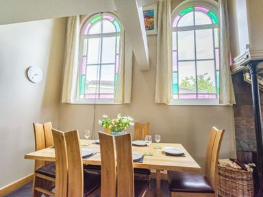 A dining area with a wooden table set with plates and glasses near stained glass windows at The New Chapel Great Hatfield near Hornsea