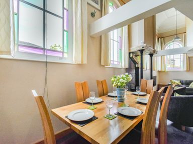 A dining table set with plates glasses and a vase with flowers in a room with large windows and wooden chairs at The New Chapel in Great Hatfield near Hornsea