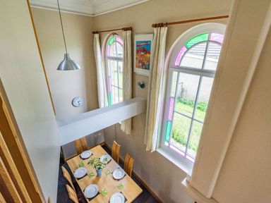 A dining room with a wooden table set for six under arched windows with stained glass at The New Chapel in Great Hatfield near Hornsea