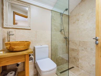 A bathroom with a wooden sink, a white toilet, a shower area with glass partition and tiled walls at The New Chapel in Great Hatfield near Hornsea