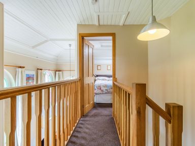 A hallway with wooden railings and a hanging lamp leading to a bedroom with a floral bedspread at The New Chapel in Great Hatfield near Hornsea