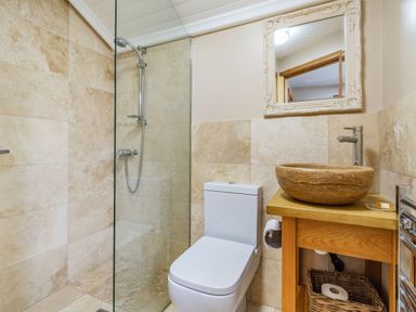 A bathroom with a shower area, toilet, wooden vanity with stone basin, and mirror at The New Chapel in Great Hatfield near Hornsea