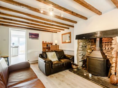 A living room with two leather sofas a stone fireplace wooden beams on the ceiling and a wooden cabinet at 3 Tyn Y Mynydd in Penmachno