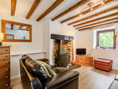 A living room with a black leather sofa stone fireplace wooden beams and a small tv at 3 Tyn Y Mynydd in Penmachno