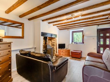 A living room with leather sofas a fireplace wooden beams a small television and a window at 3 Tyn Y Mynydd in Penmachno
