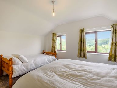 A bedroom with two wooden beds white bedding and windows with patterned curtains at 3 Tyn Y Mynydd in Penmachno