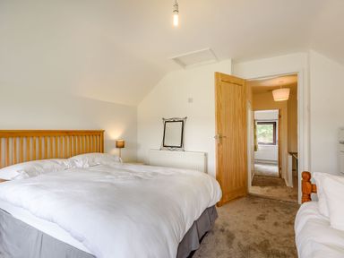 A bedroom with a double bed white bedding a wooden headboard a bedside lamp an open wooden door and a mirror on the wall at 3 Tyn Y Mynydd in Penmachno