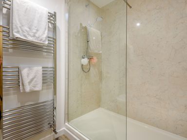 A shower area with a glass door a showerhead and towels on a chrome towel rail at 3 Tyn Y Mynydd in Penmachno