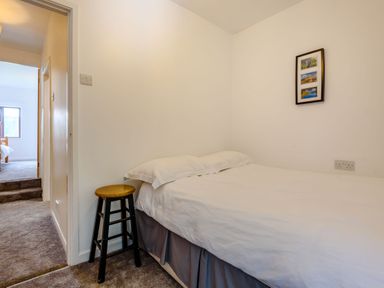A small bedroom with a single bed a wooden stool a framed picture on the wall and a view into an adjacent room at 3 Tyn Y Mynydd in Penmachno