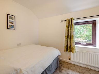 A small bedroom with a bed white walls a window with green patterned curtains and a framed picture on the wall at 3 Tyn Y Mynydd in Penmachno