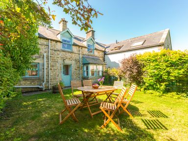 A stone cottage with blue window frames and door a wooden table with six chairs on the grass in the garden at Townfoot Cottage Elsdon near Otterburn