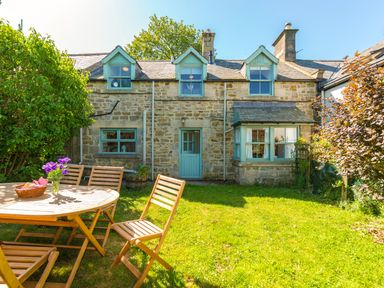 A stone cottage with blue trim windows a blue door and a wooden outdoor table with chairs on grass at Townfoot Cottage Elsdon near Otterburn