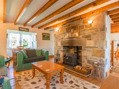 A living room with a wood stove fireplace a wooden coffee table green sofas and wooden beams on the ceiling at Townfoot Cottage Elsdon near Otterburn