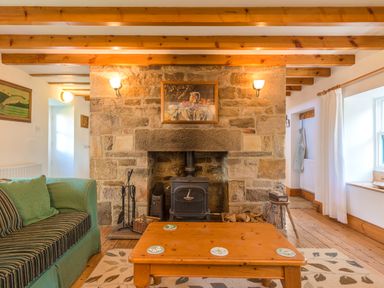 A living room with a stone fireplace wooden beams on ceiling a wooden coffee table and a green striped sofa at Townfoot Cottage Elsdon near Otterburn