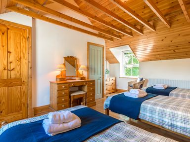 A bedroom with two single beds with blue blankets a wooden dressing table with two lamps a wicker chair a window and wooden ceiling at Townfoot Cottage Elsdon near Otterburn