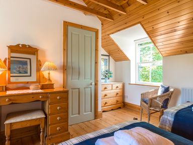 A bedroom with wooden furniture including a dressing table chest of drawers and a chair by the window at Townfoot Cottage Elsdon near Otterburn