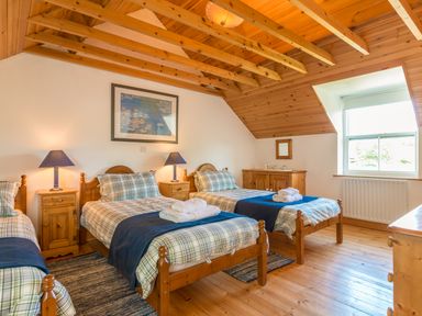 A bedroom with three single wooden beds two bedside tables with lamps a wooden dresser and a window at Townfoot Cottage Elsdon near Otterburn