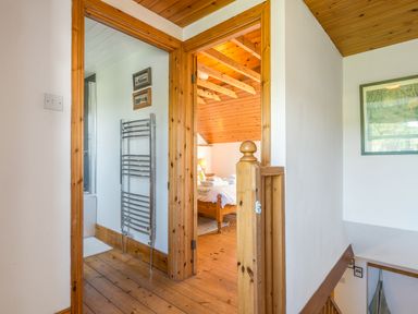 A hallway with wooden floors and doors leading to a bathroom with a towel radiator and a bedroom with a wooden bed at Townfoot Cottage Elsdon near Otterburn