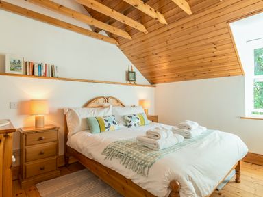 A bedroom with a wooden bed large window wooden ceiling and bedside tables with lamps at Townfoot Cottage Elsdon near Otterburn