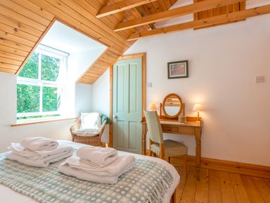A bedroom with a bed with folded towels a wicker chair by a window and a wooden dressing table with a chair at Townfoot Cottage Elsdon near Otterburn