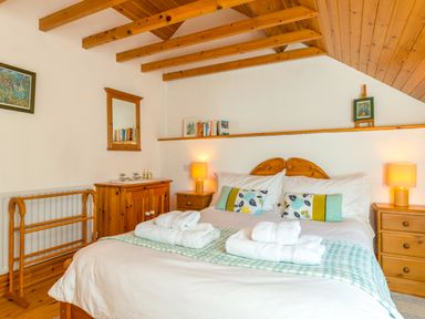 A bedroom with a double bed white linens and folded towels wooden furniture and exposed wooden beams at Townfoot Cottage Elsdon near Otterburn